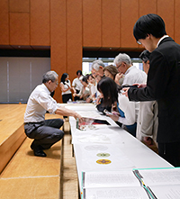 國華清話会 第2回トークイベント 講演後、会員にステンドグラス素材を説明する志田政人氏〈長机を挟んで左〉